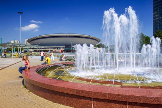 Foto di una fontana a Katowice. Sullo sfondo, i passanti si godono una bella giornata di sole.